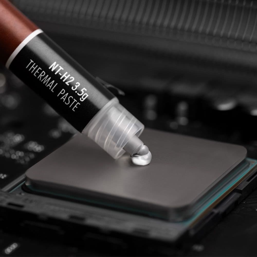 A close-up shot of Noctua NT-H2 3.5g thermal paste being applied to the center of a CPU's heat spreader.